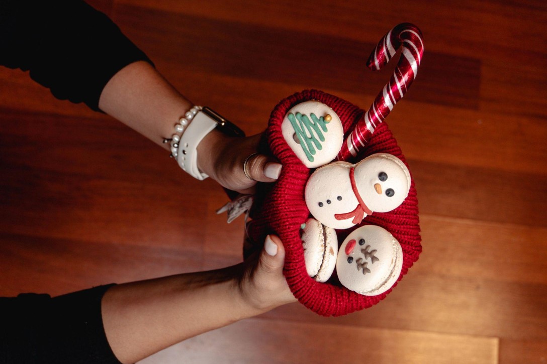 Woman holding knitted red hat with Christmas sweets inside, top view.